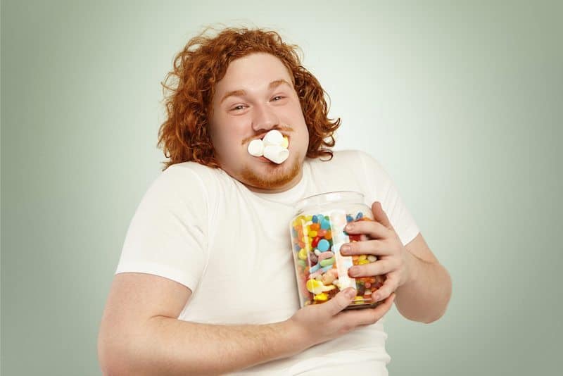 a man holding a jar of candies and marshmallows stuffed in his mouth like keyword stuffing which is a black hat technique
