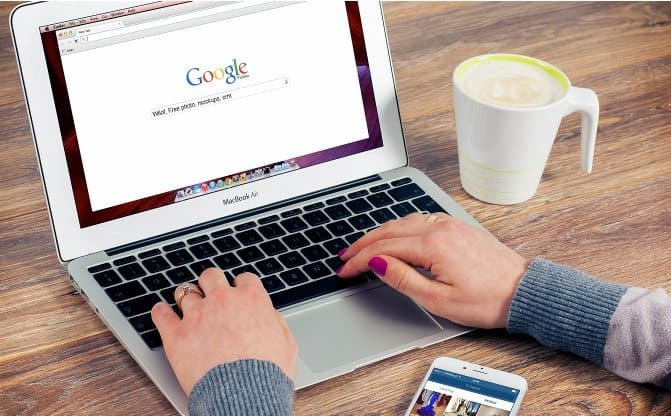 An image of a woman's hand typing on the keyboard of a laptop with a cup of coffee on the right side