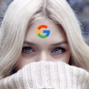 A close-up image of a face of a woman with white blonde hair and blue eyes with the logo of Google on her forehead
